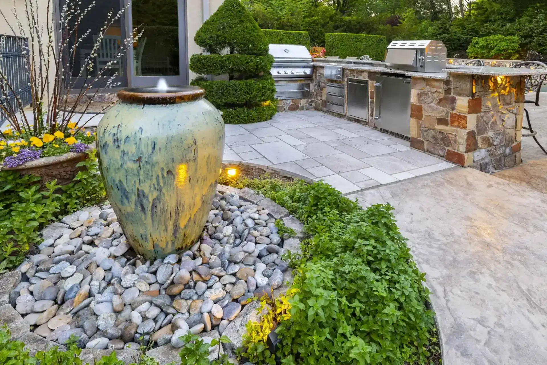 Stone water feature in a landscaped garden beside a paved patio and stone wall