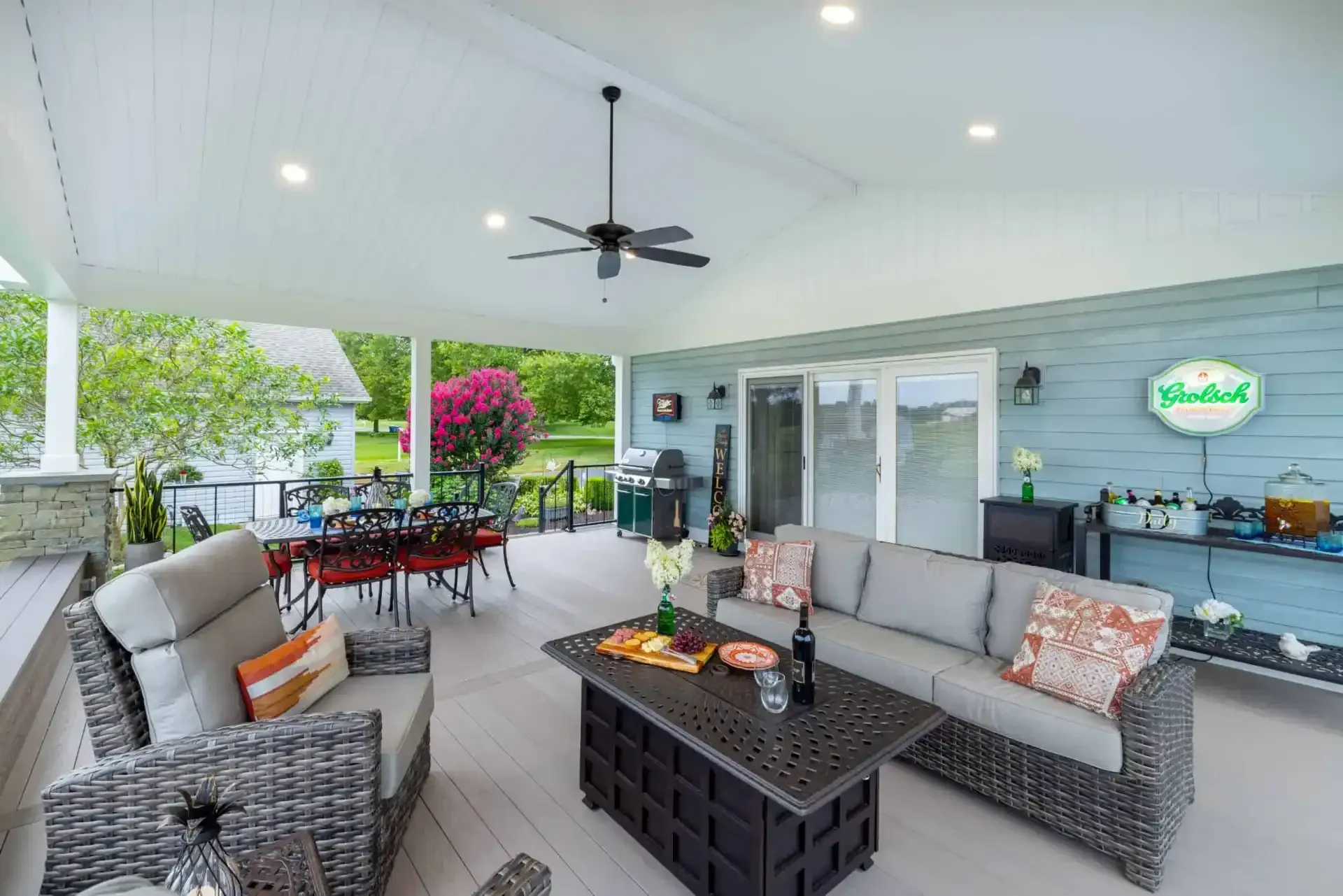 Covered patio with wicker seating, dining table, ceiling fan, and garden view