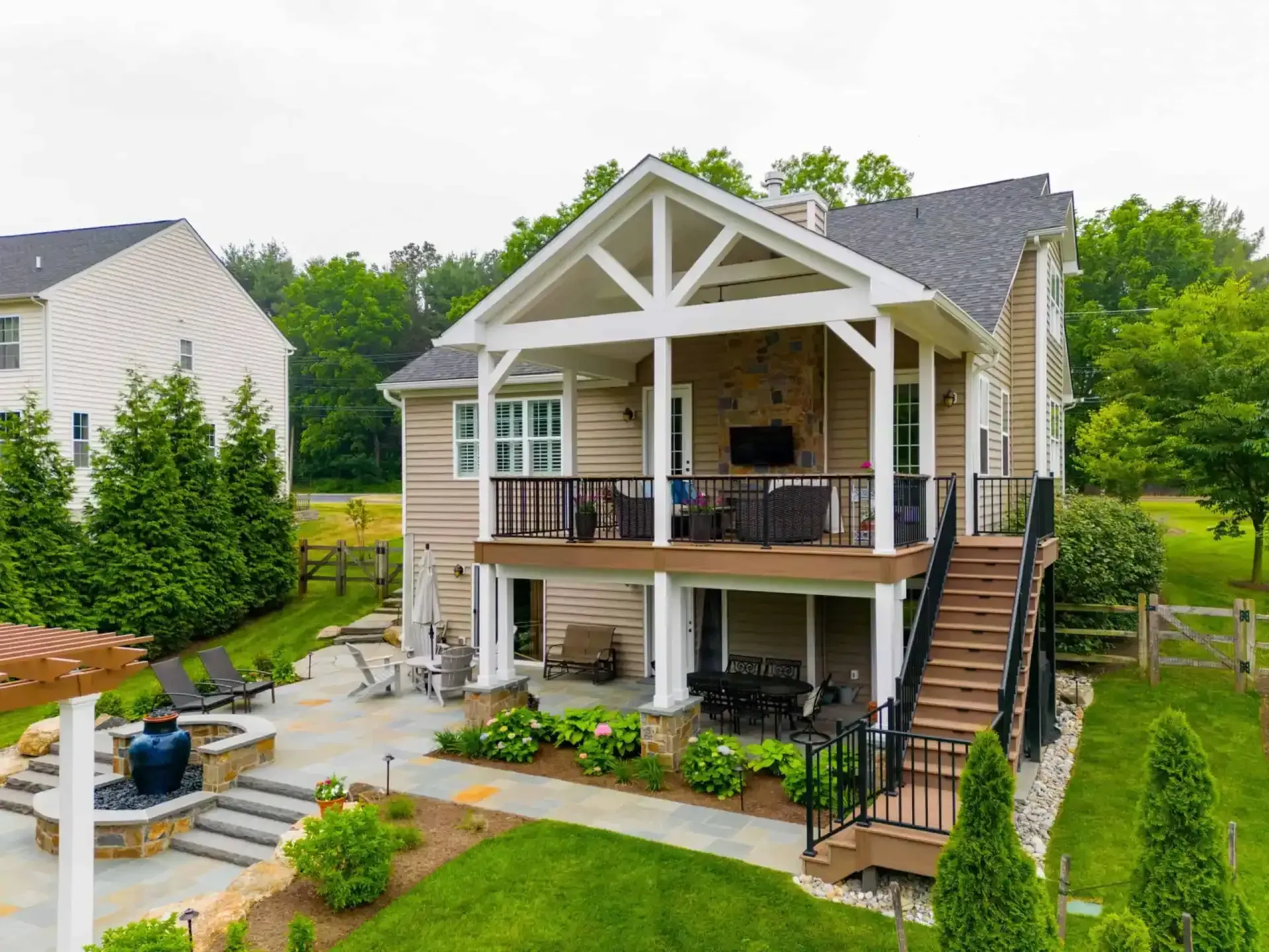Small beige house with a raised porch, black railings, and front stairs in a landscaped yard