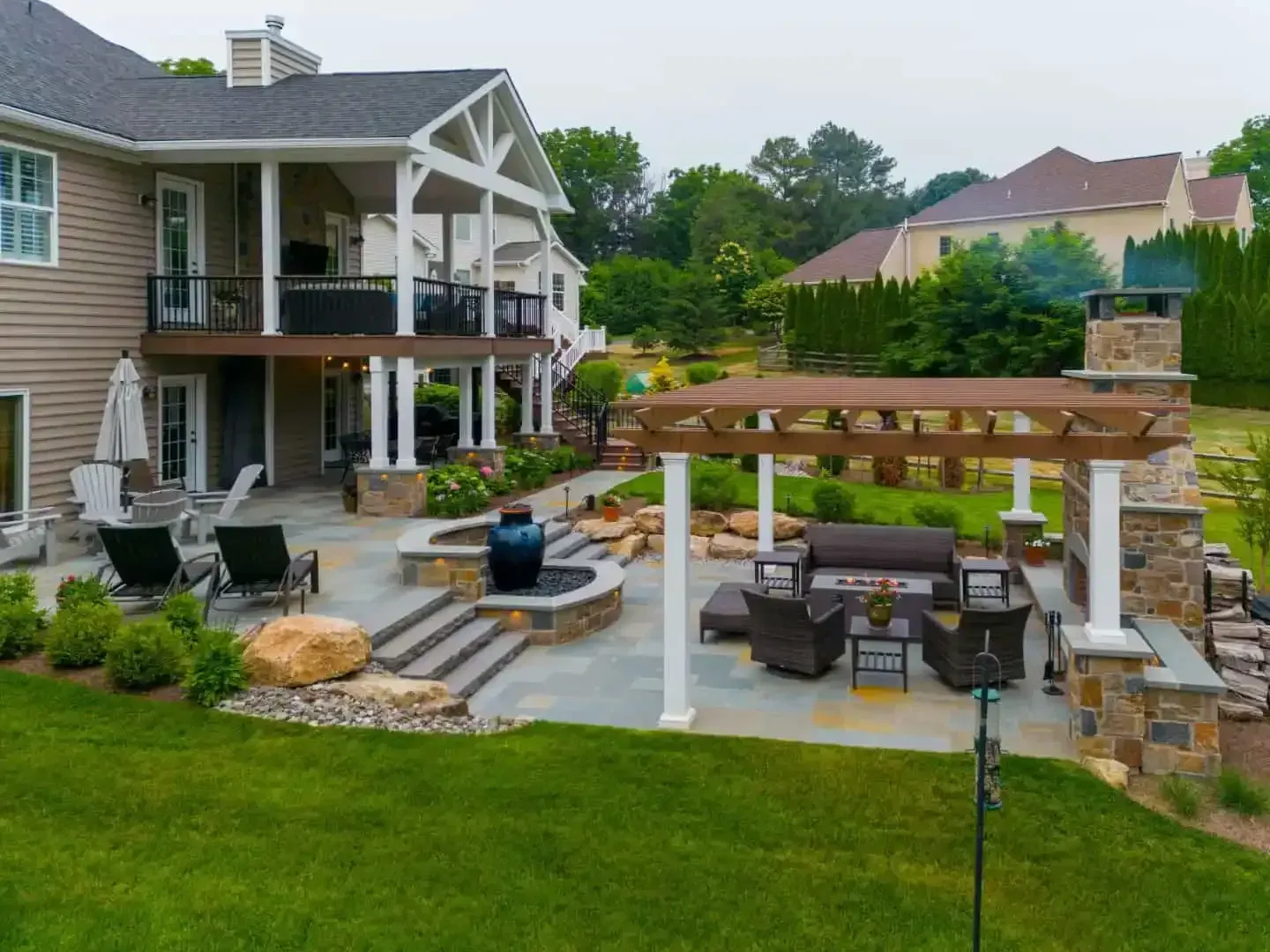Backyard patio with stone fireplace, pergola seating, and two-story house in the background