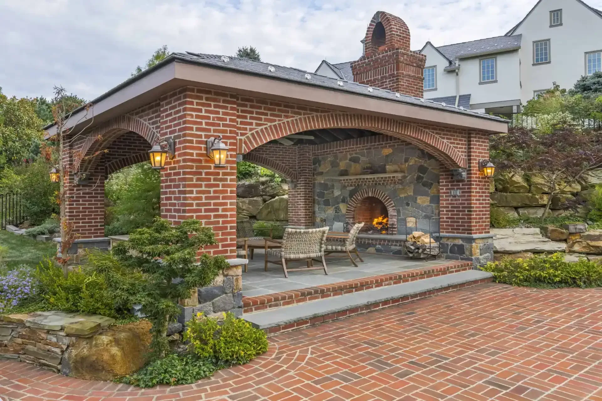 Brick outdoor fireplace pavilion with stone seating on a brick patio in a garden backyard