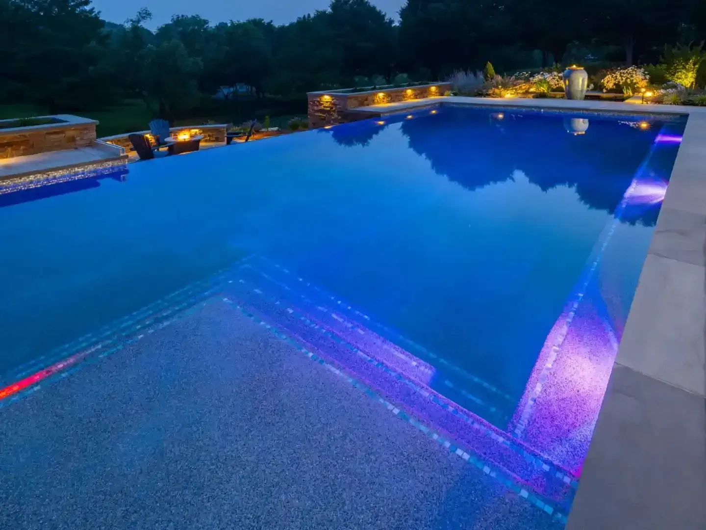 Illuminated outdoor swimming pool at dusk with blue water and purple lights along the edge