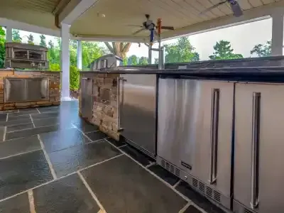 Outdoor kitchen patio with stainless steel grill and refrigerator under a covered pavilion