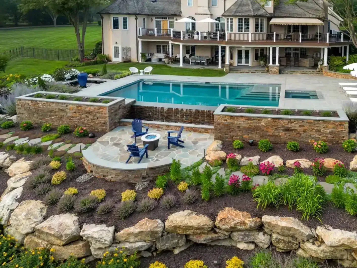 Luxury backyard with pool, stone patio, hot tub, and landscaped rock garden beside a large house