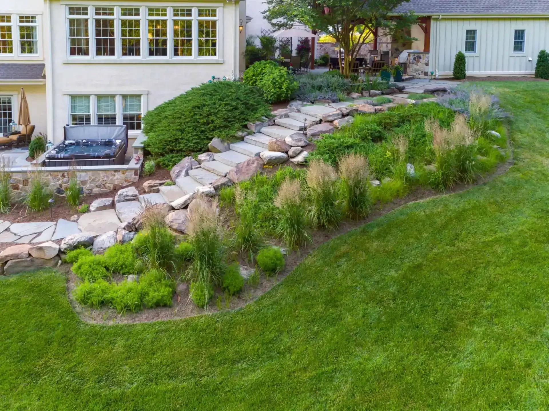 Landscaped backyard with stone path, curved retaining wall, and lush green lawn beside a house