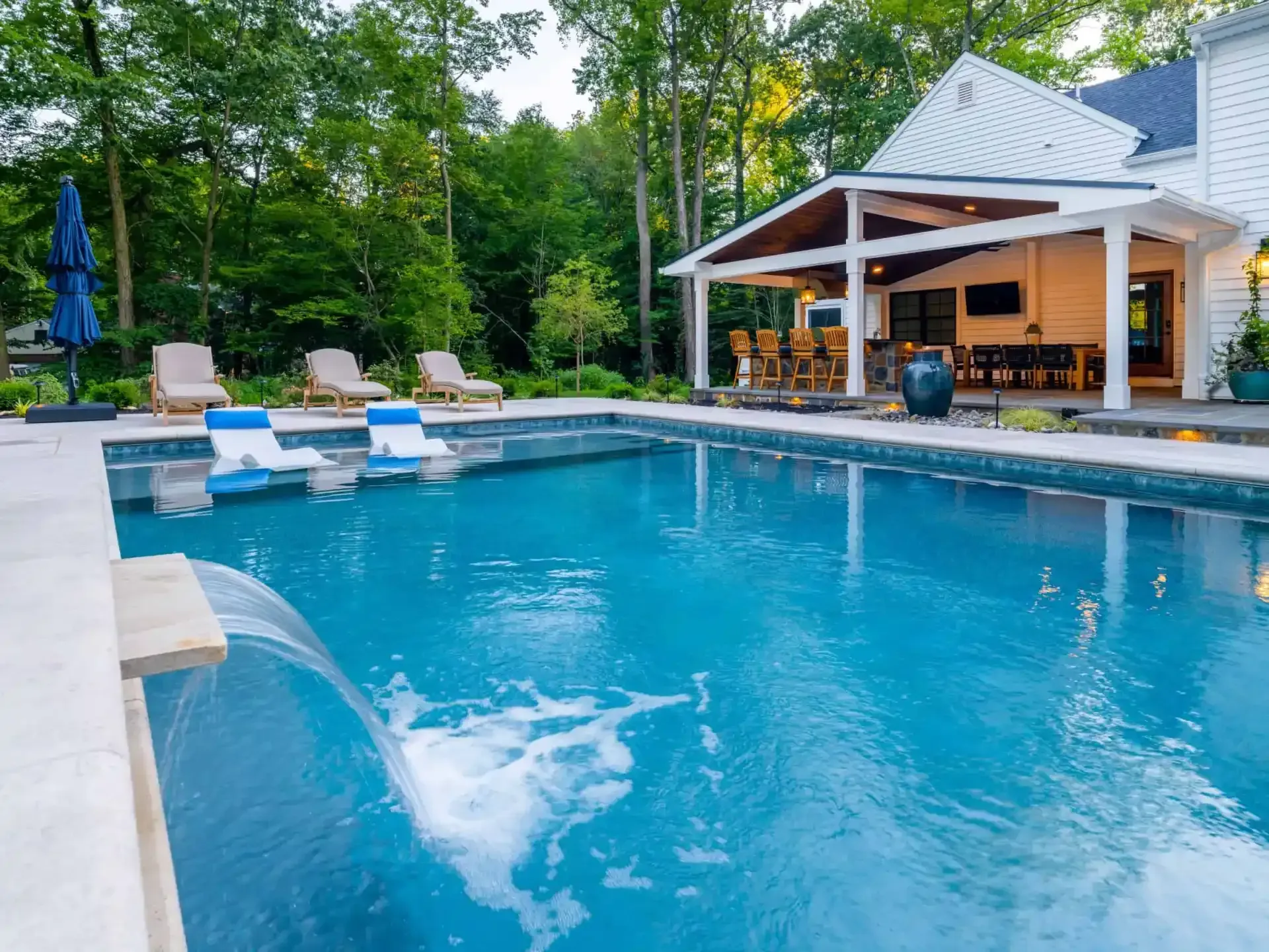 Backyard pool with blue water, lounge chairs, and a white gazebo beside trees