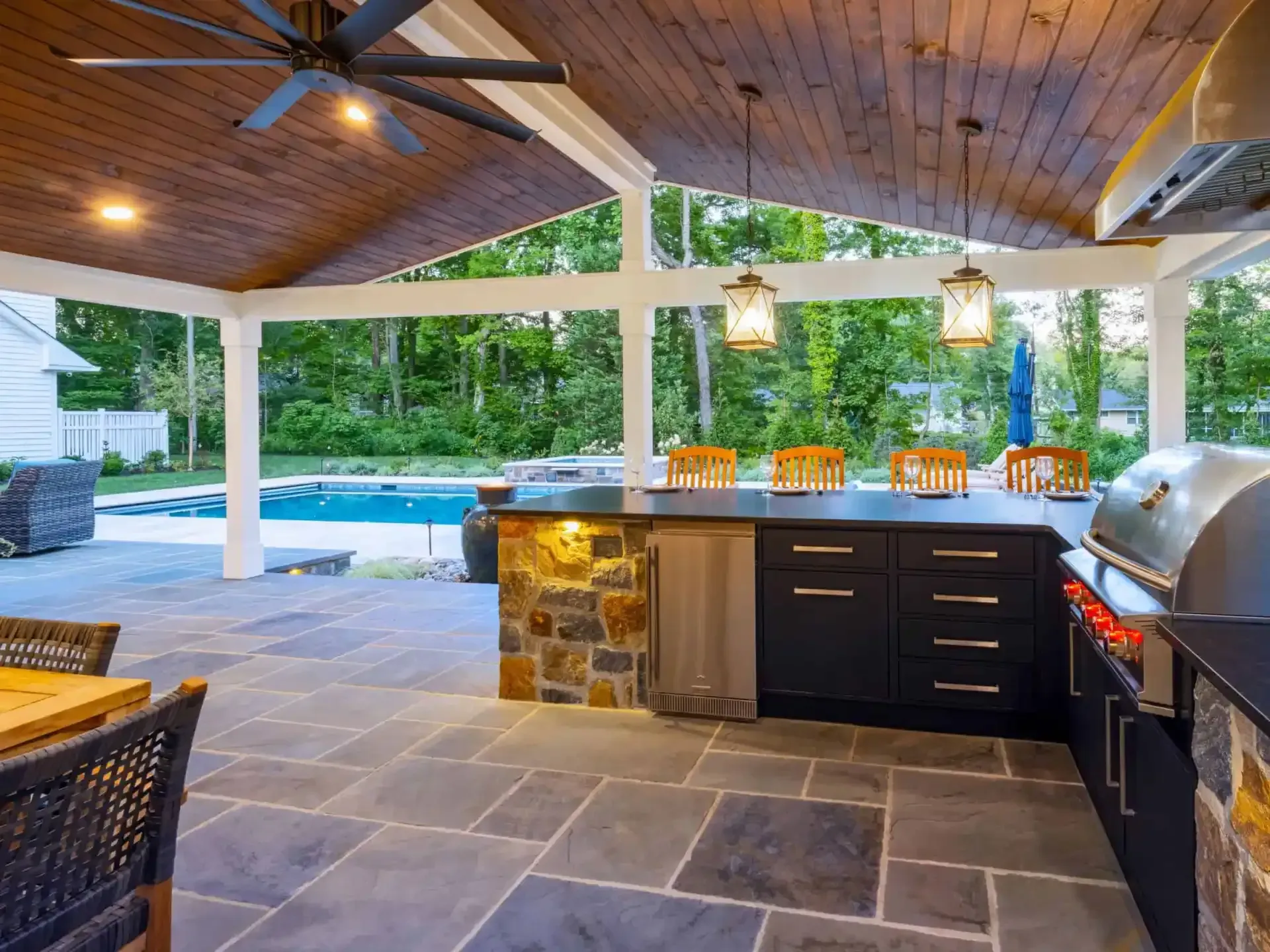 Outdoor covered patio with stone bar, grill, ceiling fans, and a pool view beyond