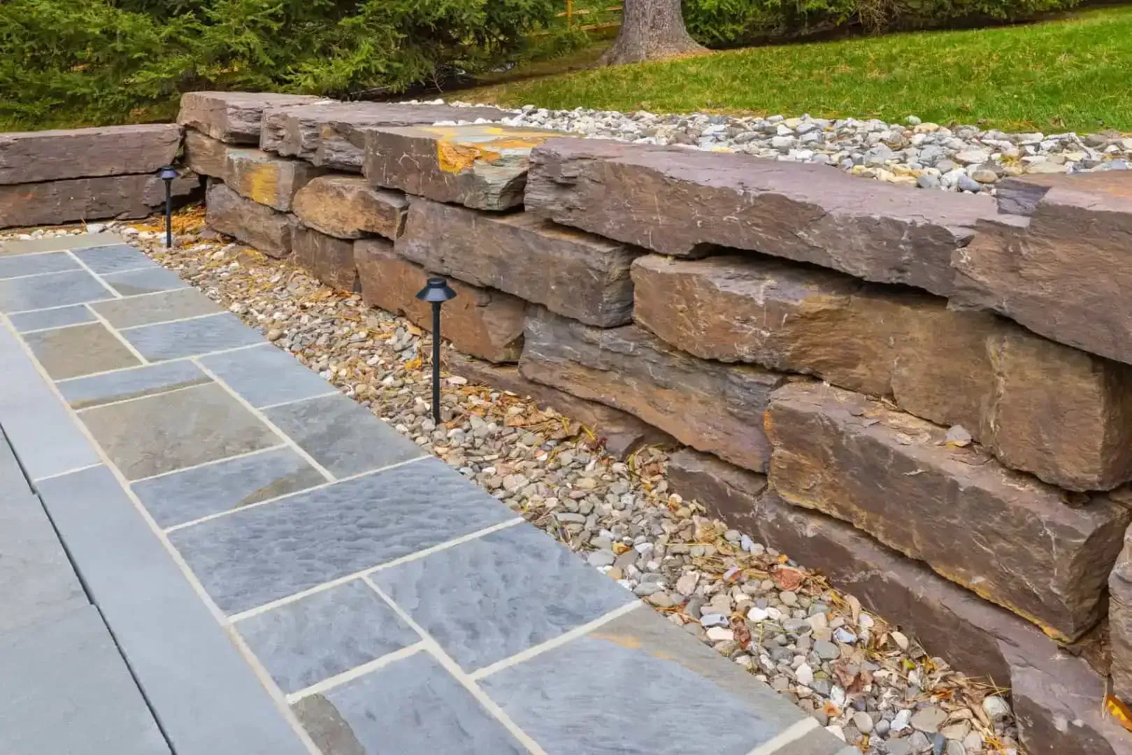 Blue stone patio with a stacked stone retaining wall and gravel border in a landscaped yard