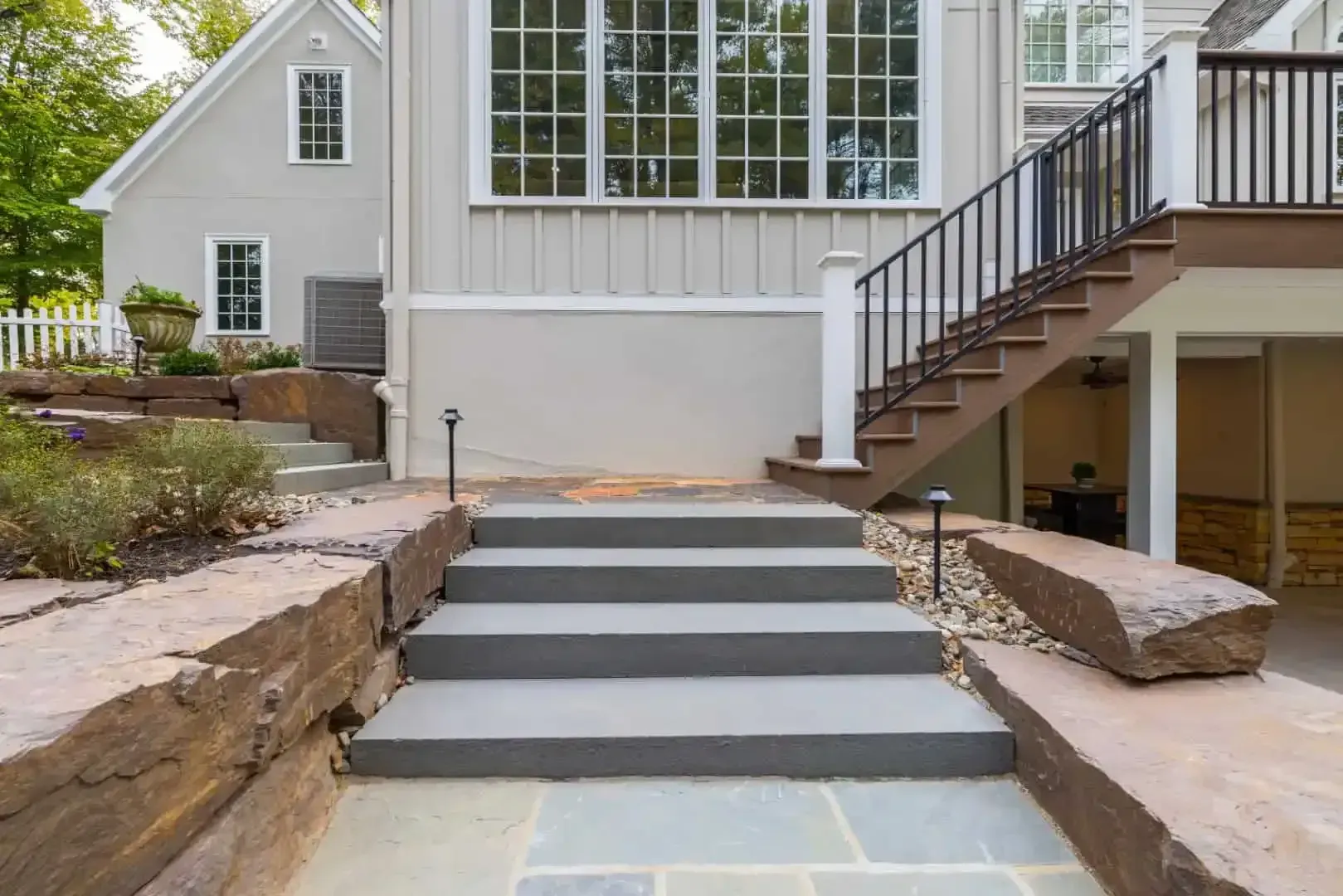 Stone steps and a side stairway leading to a white house entrance with large windows and landscaped rock borders