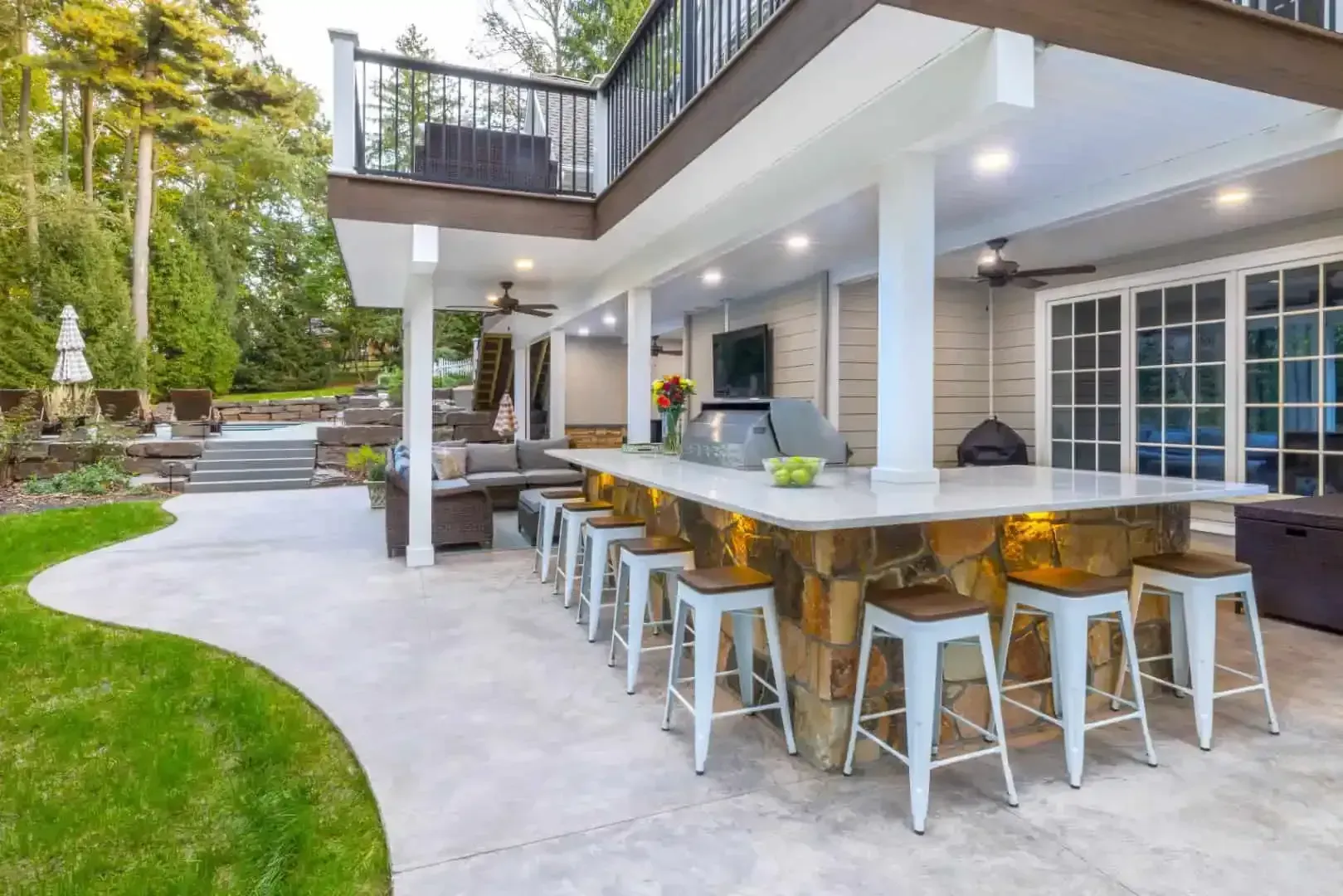 Outdoor patio with a large bar counter, stools, and a poolside seating area in a modern backyard