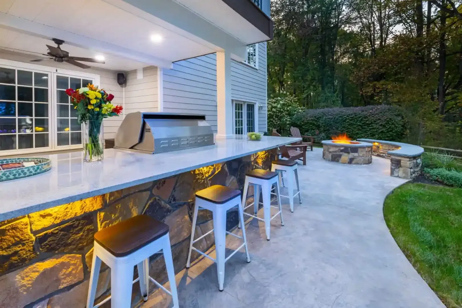 Outdoor patio with stone fire pit, bar seating, and a covered kitchen beside a modern house