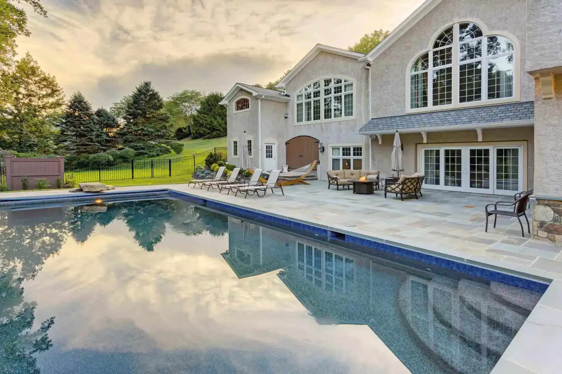 Luxury house with a backyard pool at sunset, reflecting the sky