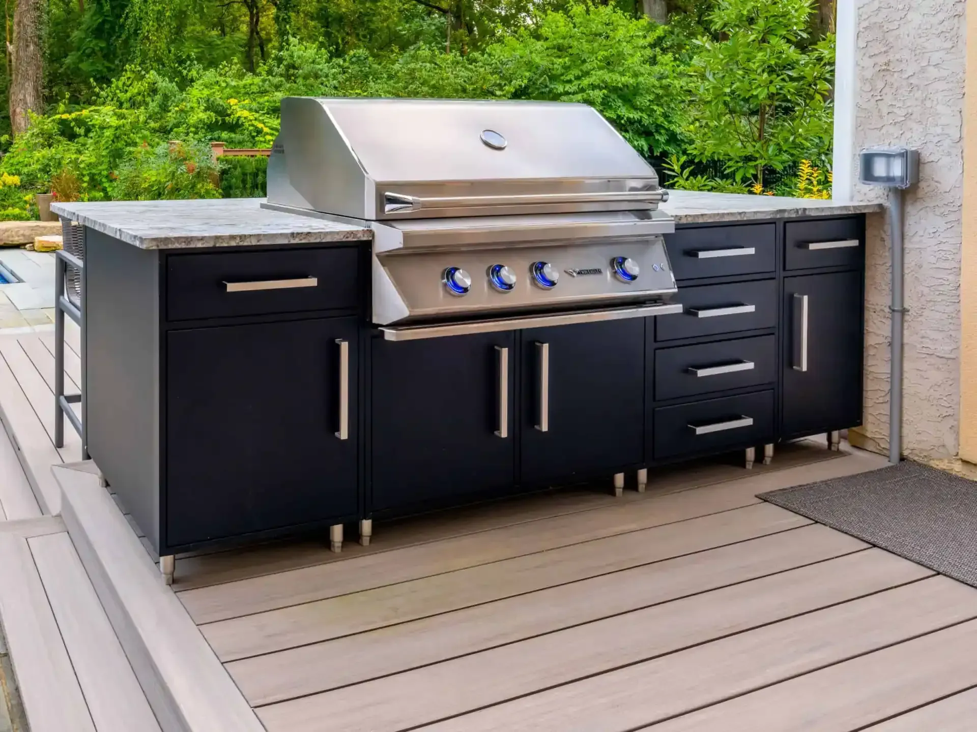 Outdoor stainless steel grill setup with black cabinets on a wooden deck
