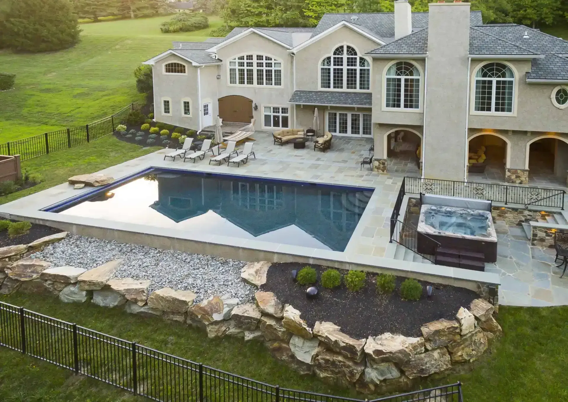Luxury house with a backyard pool, hot tub, and stone patio overlooking a landscaped lawn