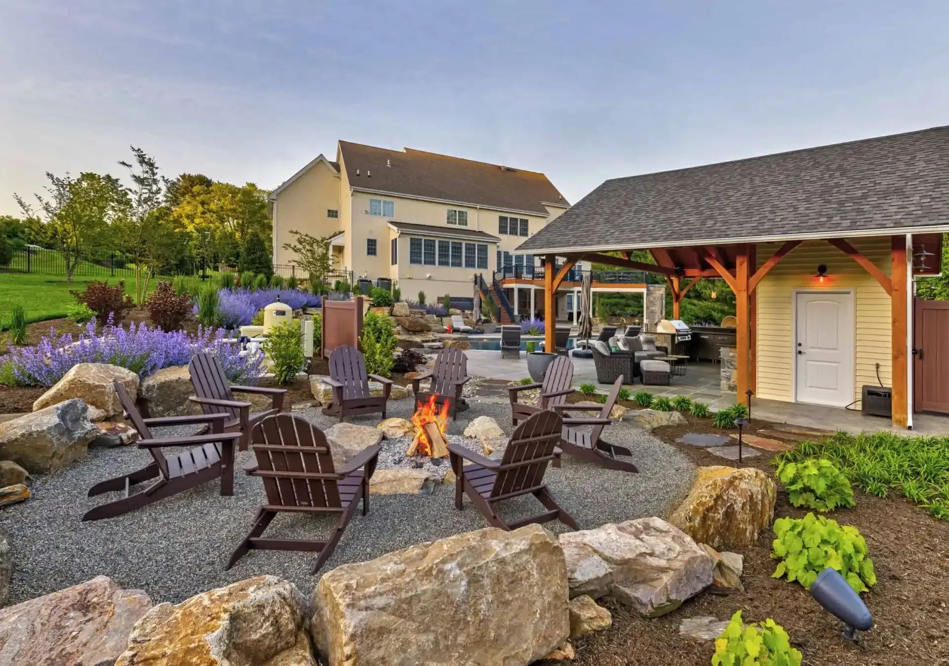 Outdoor patio with fire pit, Adirondack chairs, stone landscaping, and a covered pavilion at dusk