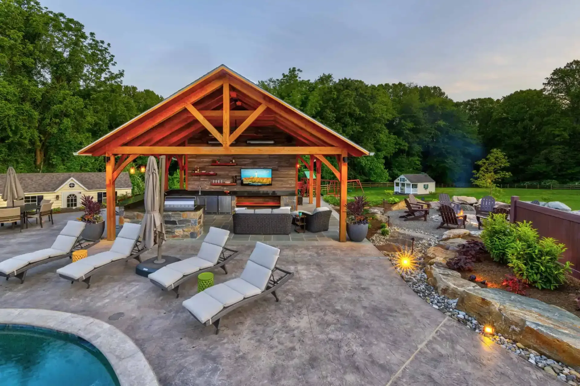 Outdoor poolside patio with cabana, lounge chairs, fire pit, and landscaped yard at dusk