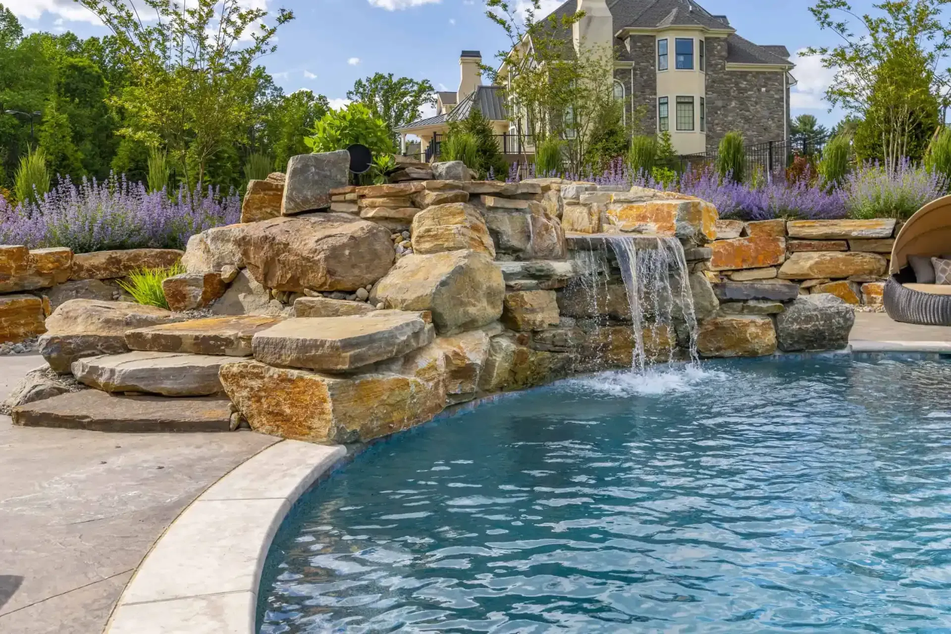 Backyard pool with stone waterfall and landscaped garden by a house