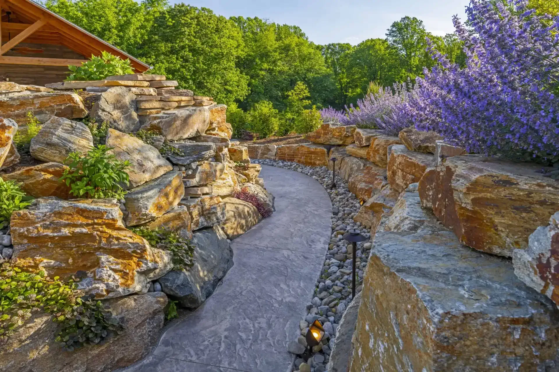Stone garden path winding between rock walls and purple flowers in a sunny landscape