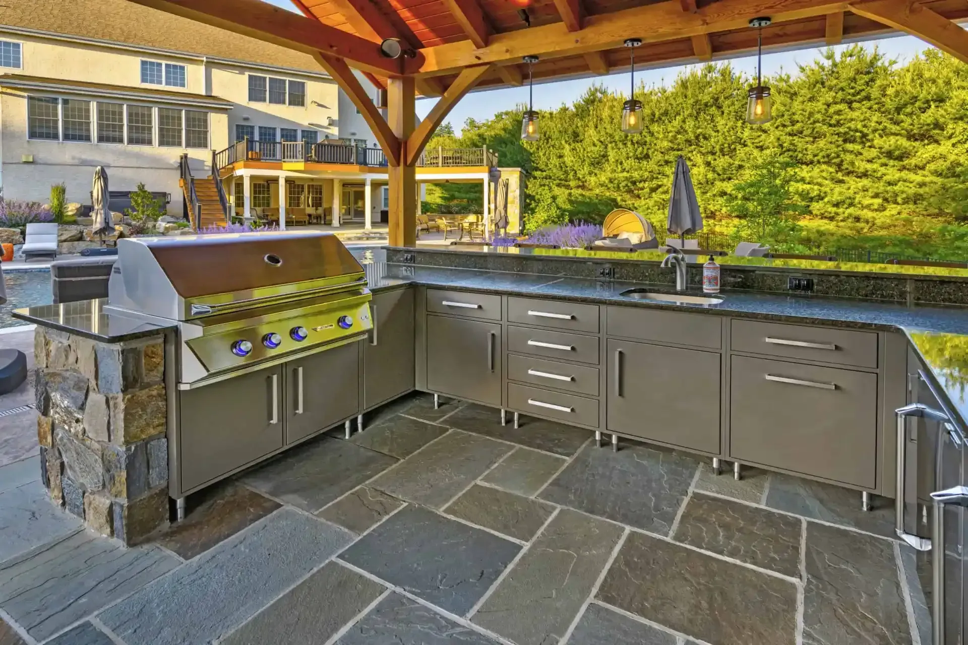 Outdoor kitchen with built-in grill, stone countertop, and cabinets under a wooden pergola