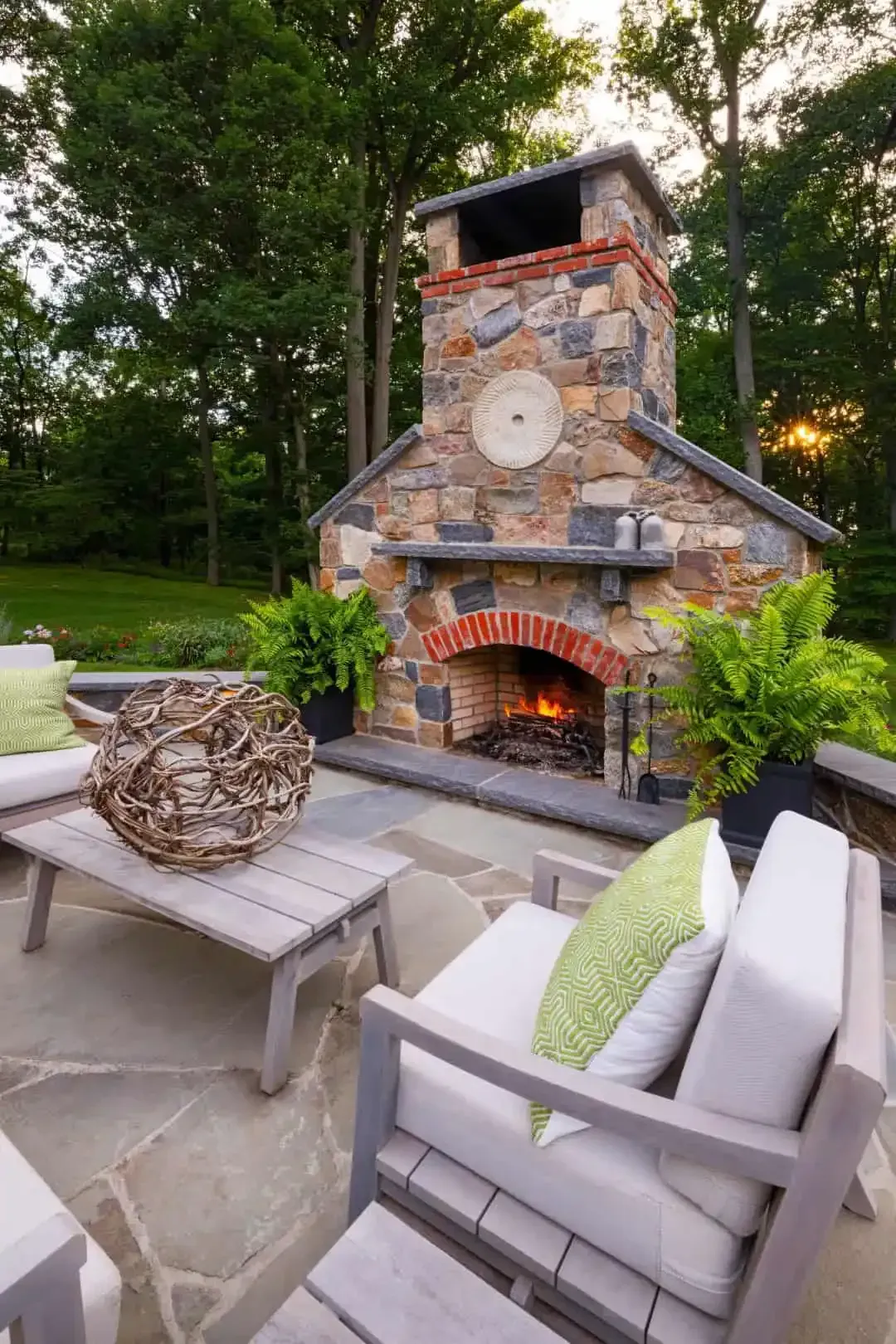 Cozy backyard patio with stone fireplace, lounge chairs, and a woven basket near lush greenery