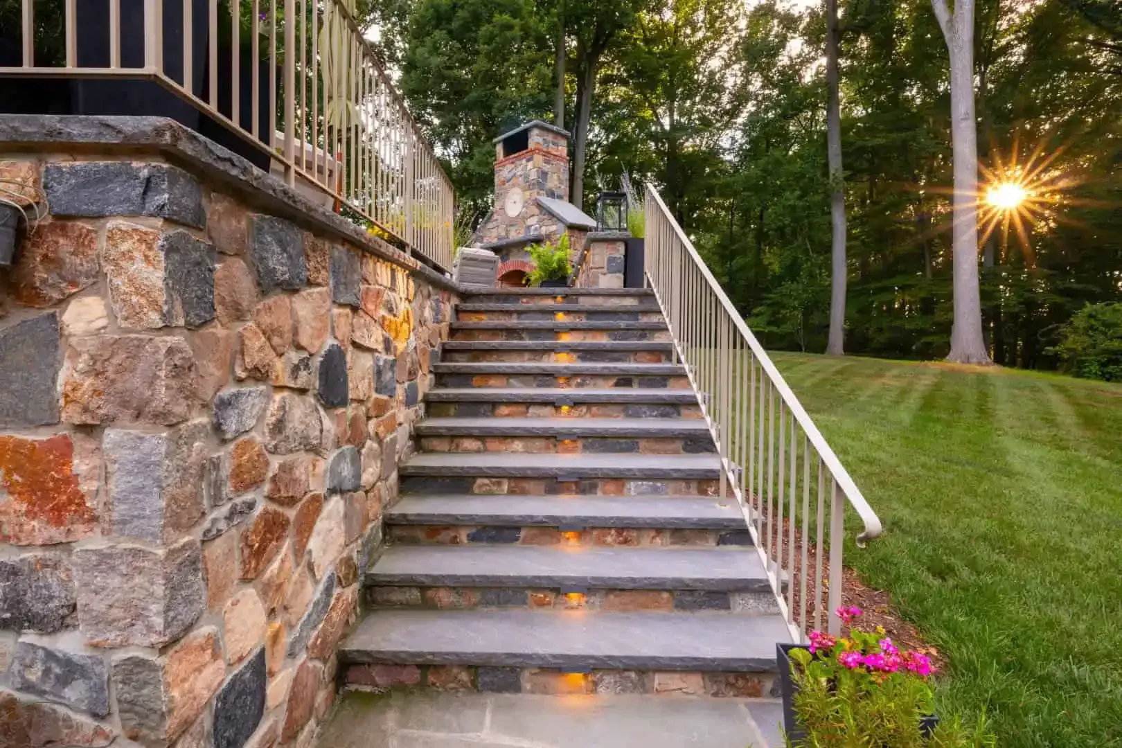 Stone stairway beside a retaining wall, leading up through a wooded yard with a sunset glow.