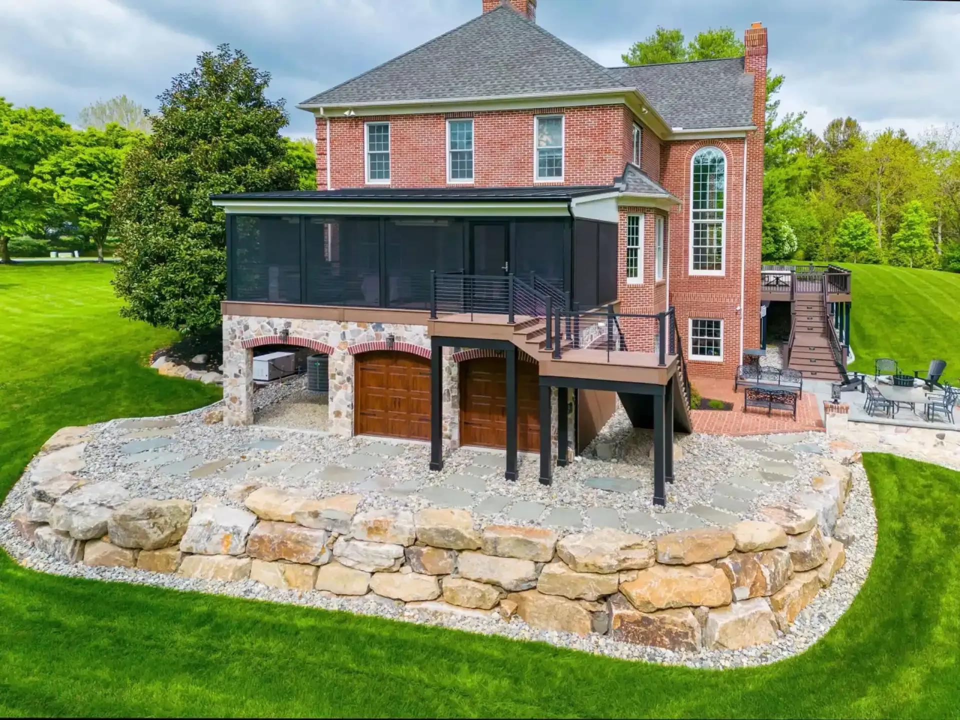 Brick house with large screened porch and stone patio in a landscaped yard