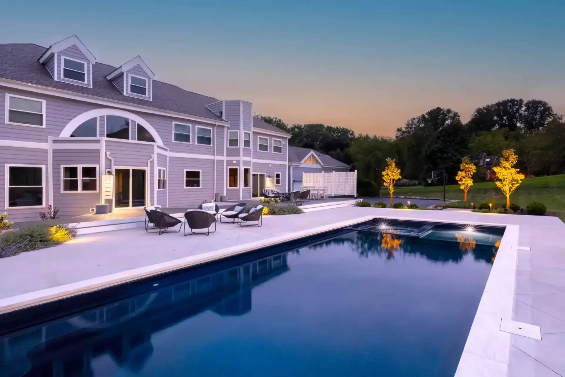 Luxury house with lit pool and patio at dusk