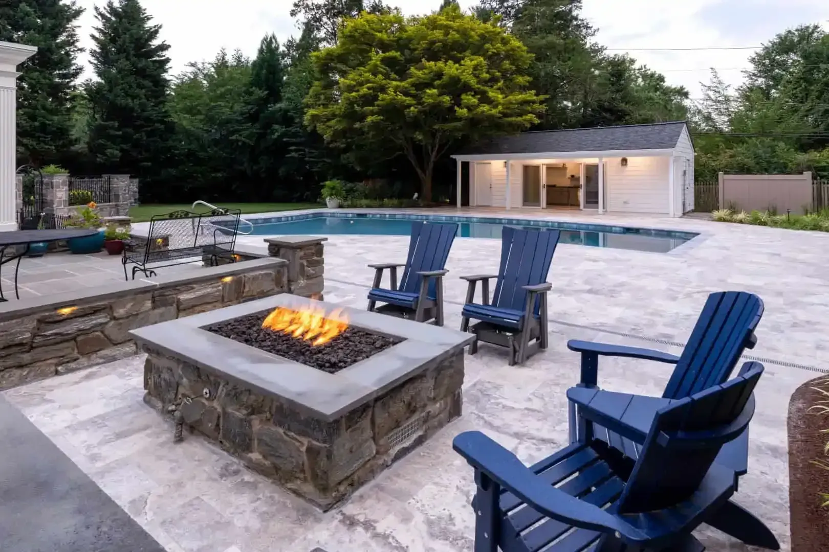 Backyard patio with fire pit, blue chairs, and a swimming pool at dusk