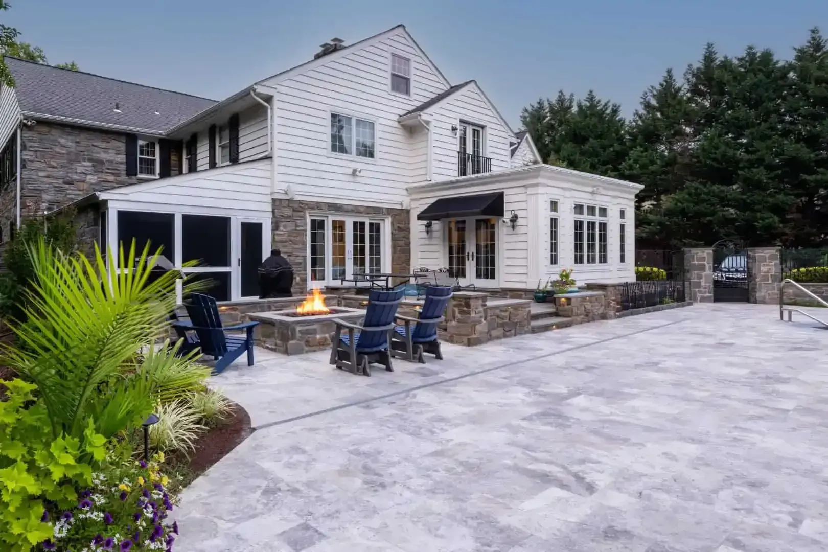 Stone patio and large white house exterior with blue chairs and potted plants.