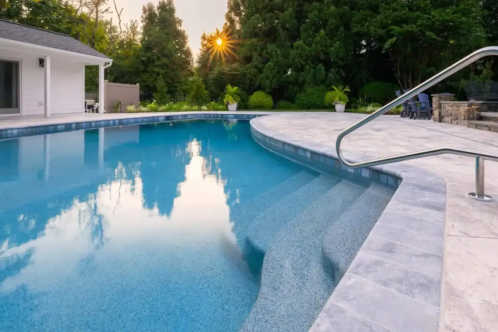 Backyard swimming pool with curved stone edge, clear blue water, and sunset reflections