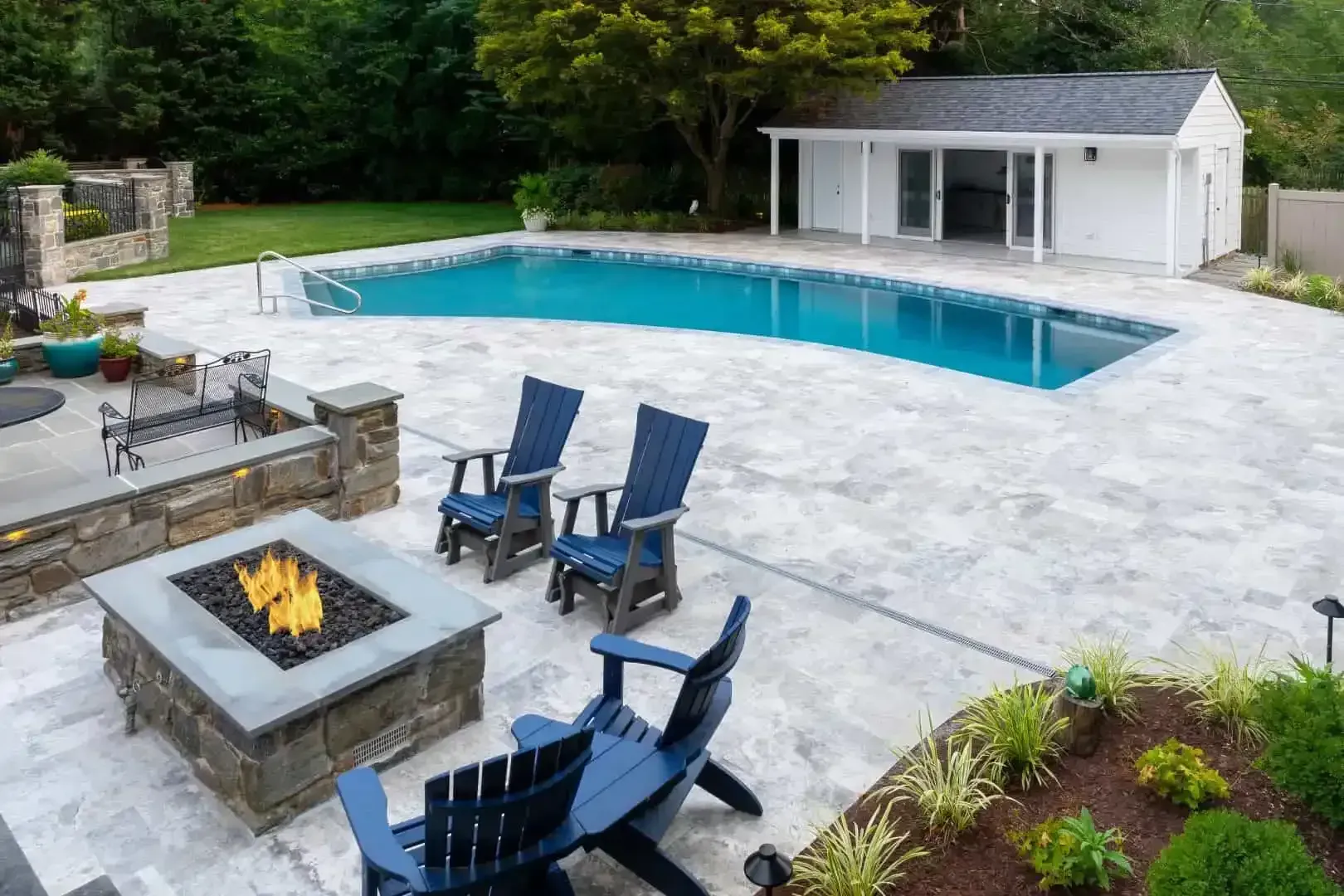 Backyard pool patio with fire pit and blue chairs beside a white pool house