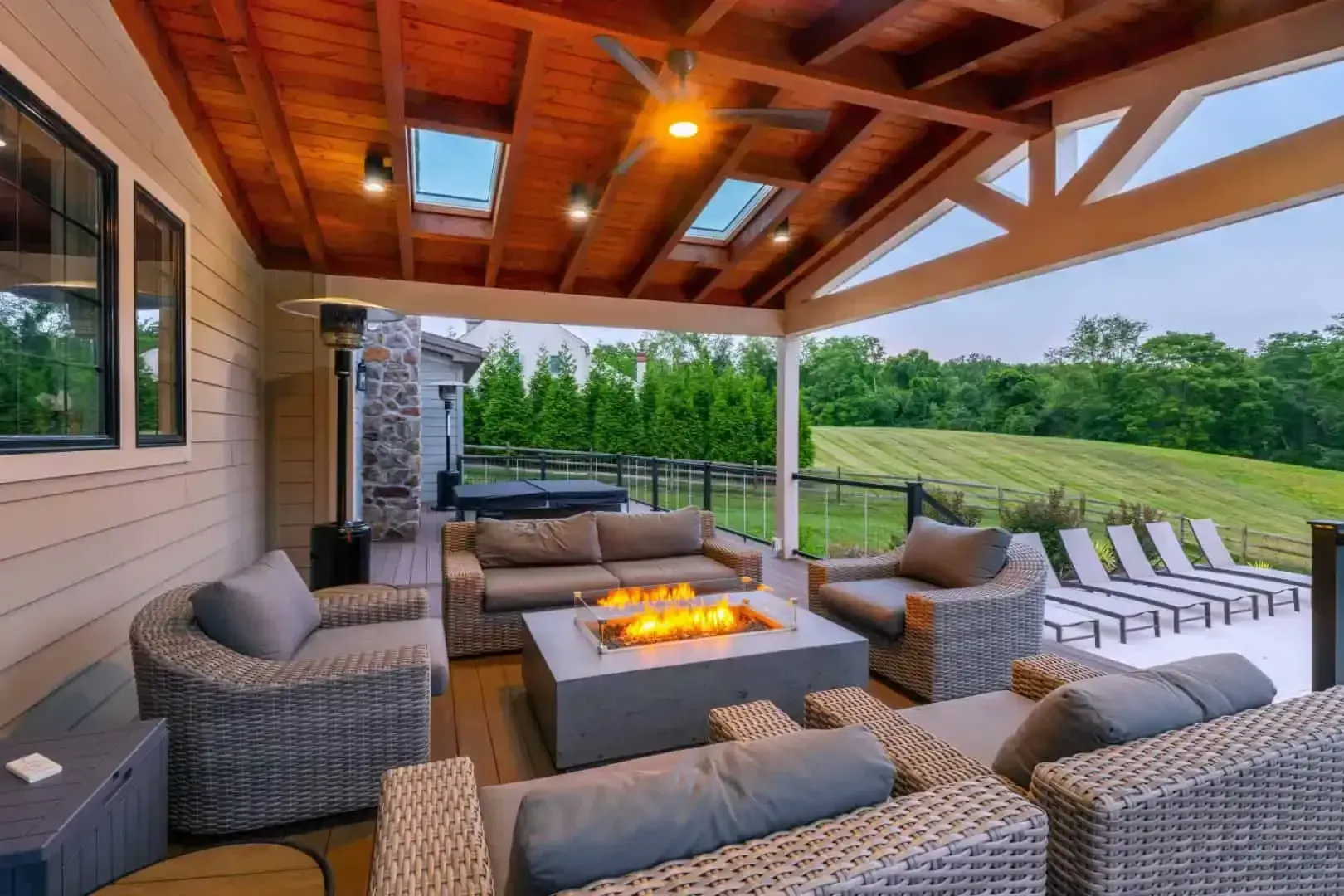 Covered patio with wicker seating, fire pit, and lounge chairs overlooking a green lawn