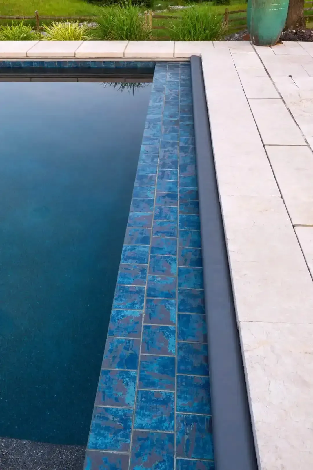 Swimming pool with blue tiled edge and light stone deck beside green lawn
