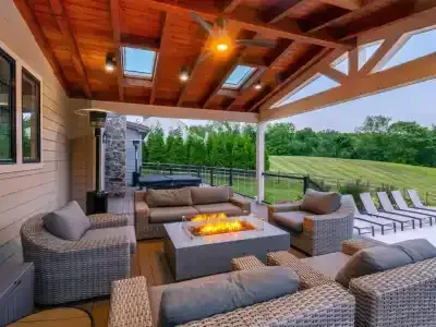 Covered patio with wicker seating around a fire pit, overlooking a grassy backyard