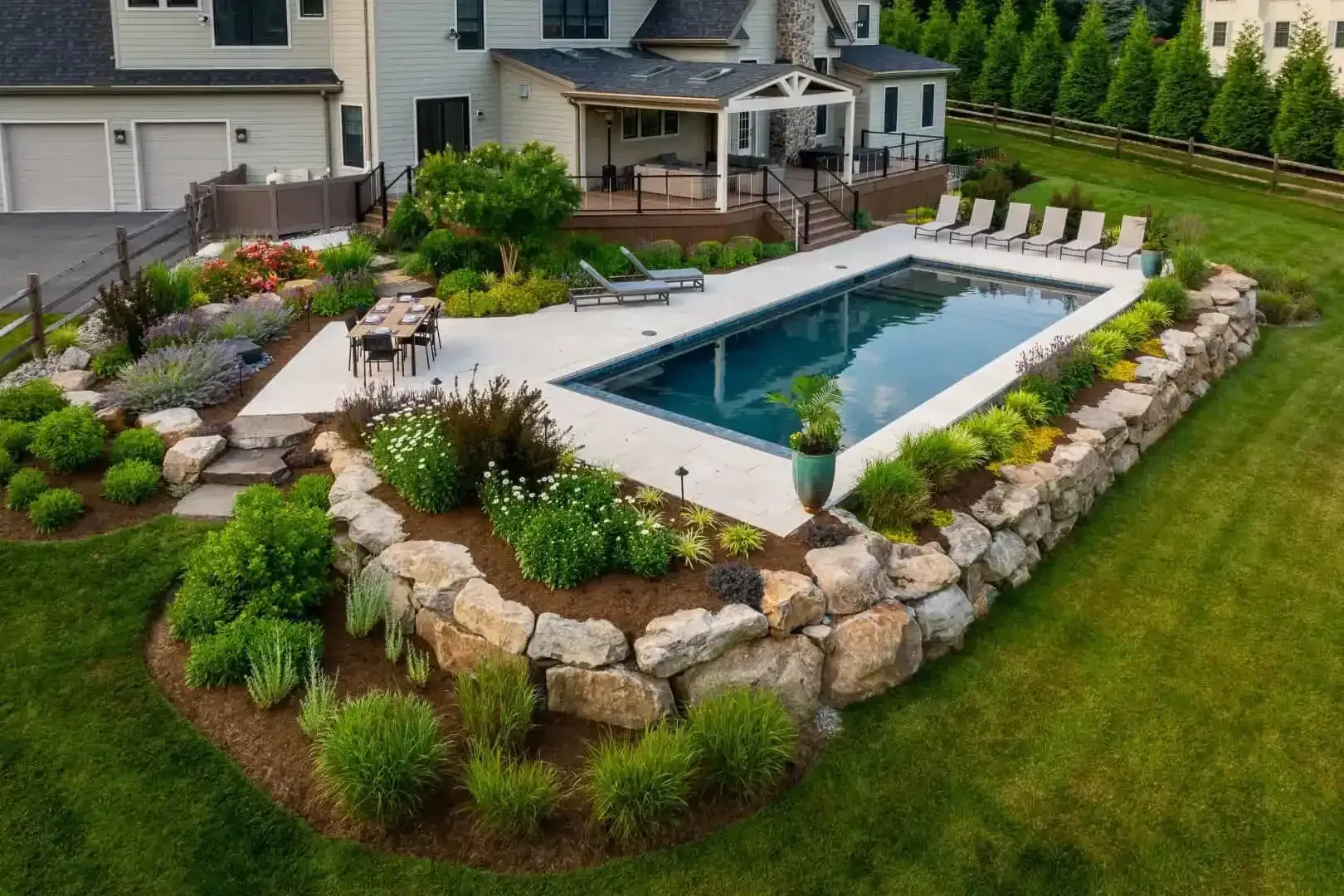 Backyard with a rectangular in-ground pool, stone landscaping, lounge chairs, and a house in the background