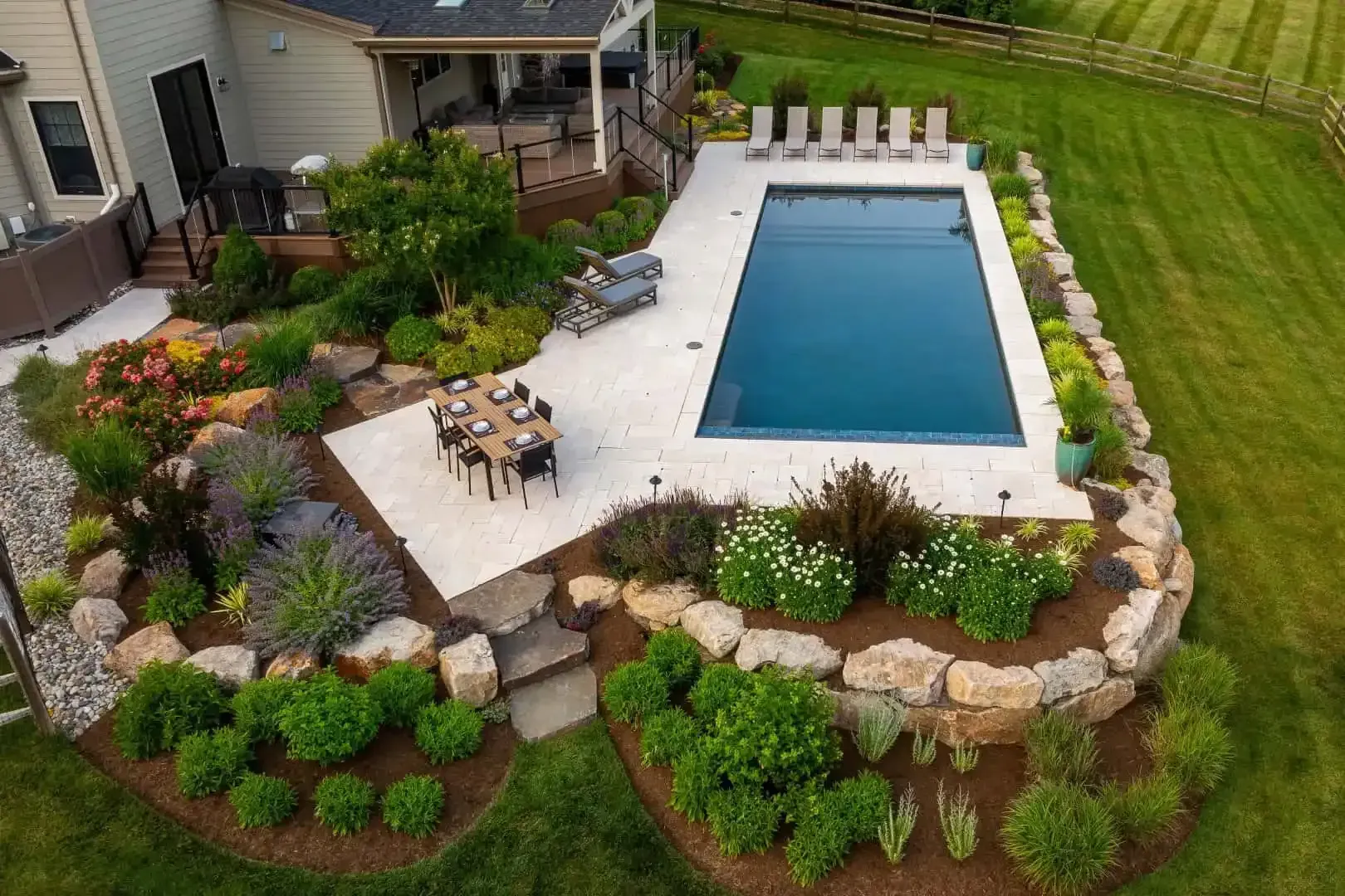 Backyard patio with rectangular in-ground pool, lounge chairs, and landscaped stone border