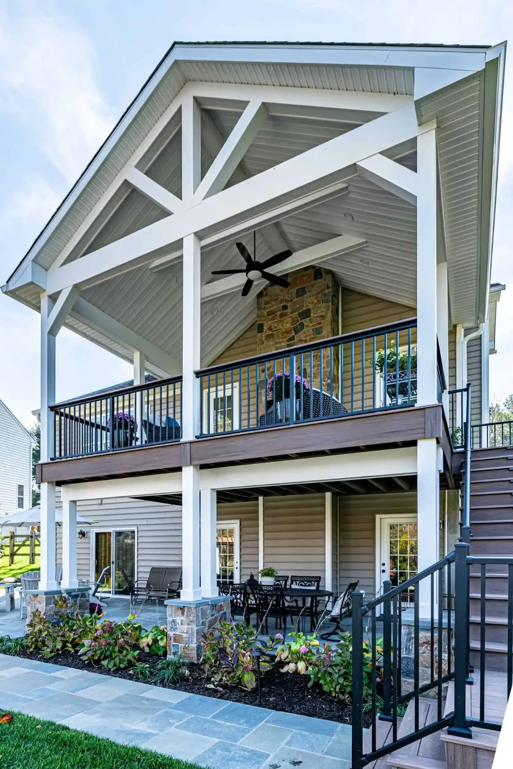 Two-story house with a large covered porch, white beams, stairs, and outdoor seating with ceiling fans
