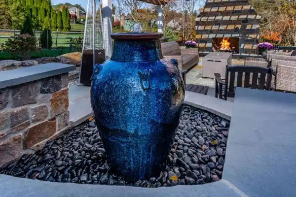 Blue ceramic fountain in a landscaped outdoor patio with stone borders and seating area
