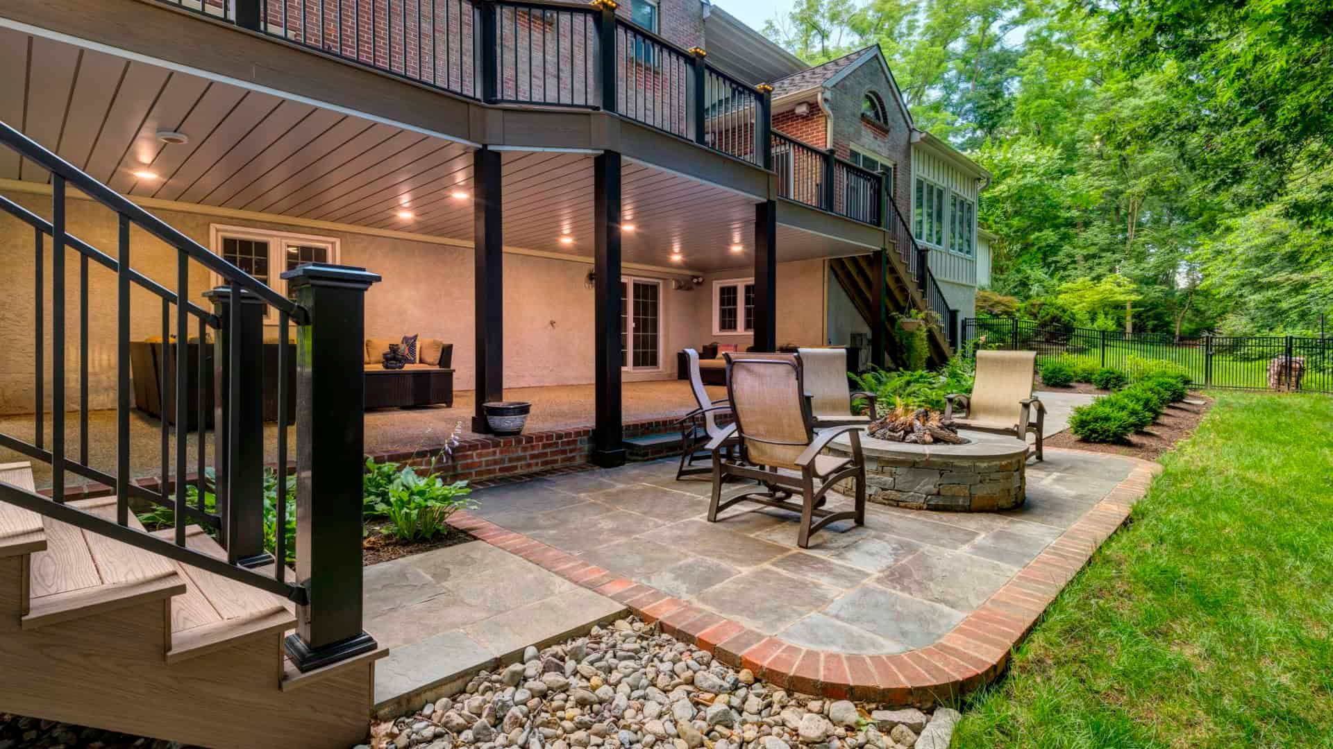 Backyard patio with deck stairs, seating area, fire pit, and string lights beside a landscaped lawn