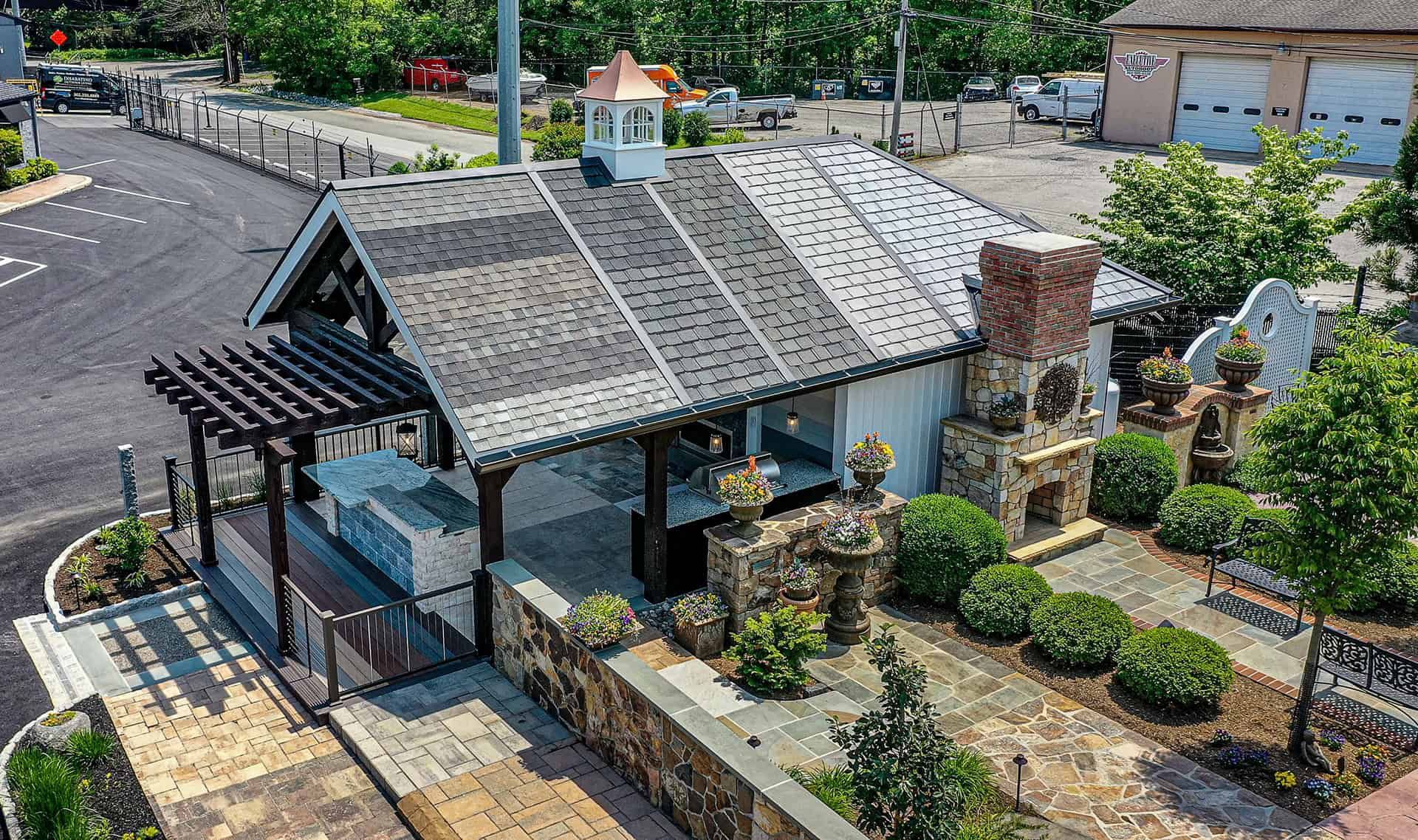 Aerial view of a small stone cottage with a garden, chimney, and adjacent parking lot