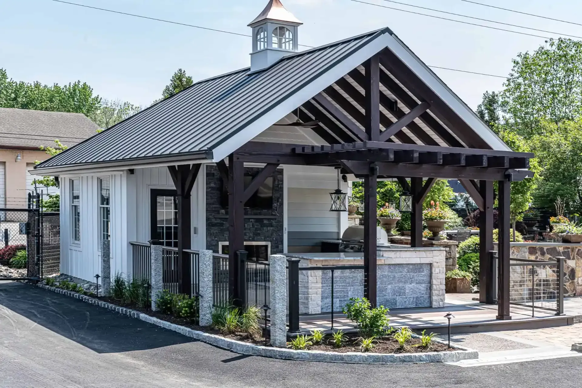 Small pavilion with a dark metal roof, white walls, and open porch in a paved outdoor area