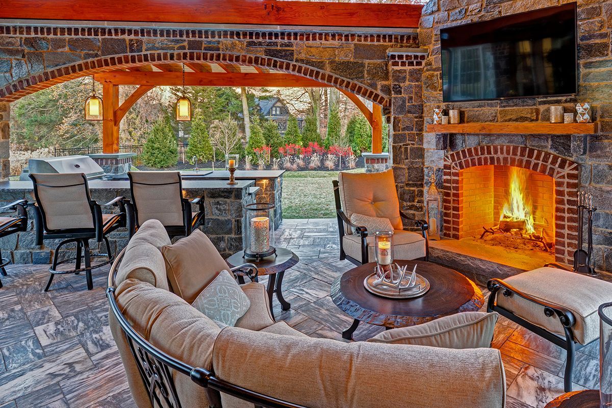 Covered patio with stone fireplace, wicker seating, and dining table overlooking a garden
