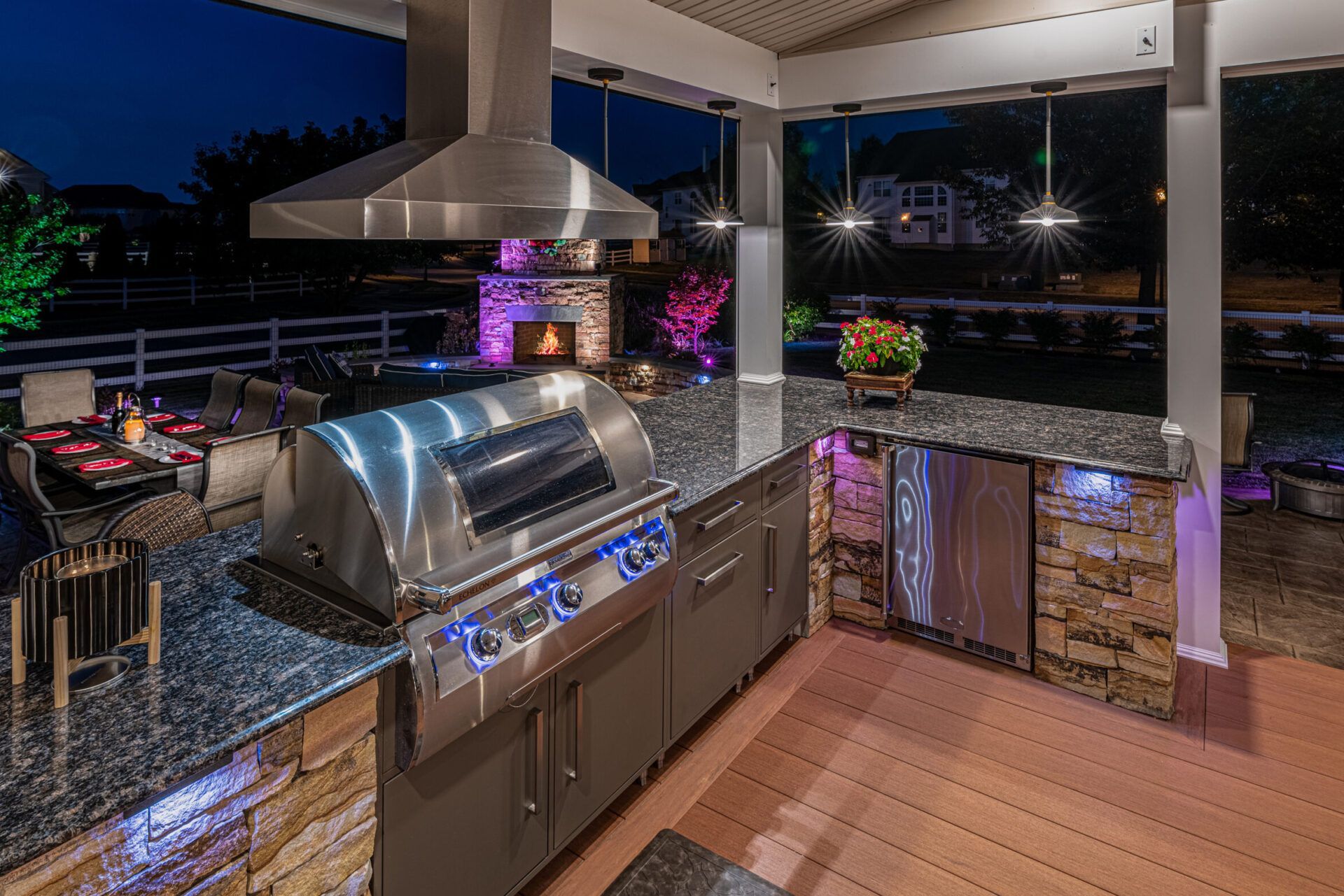 Modern outdoor kitchen with stainless grill, granite counters, and covered patio at dusk