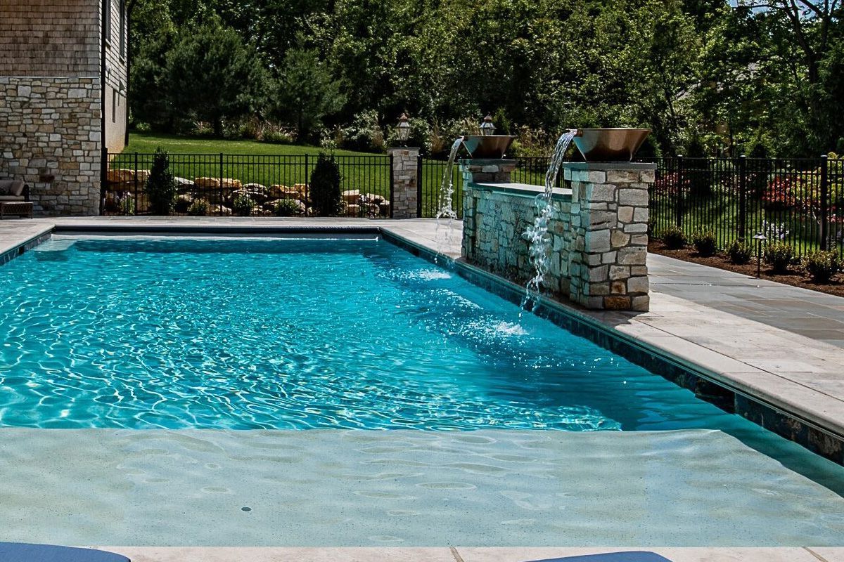 Backyard swimming pool with bright blue water, stone fountain feature, and patio surround