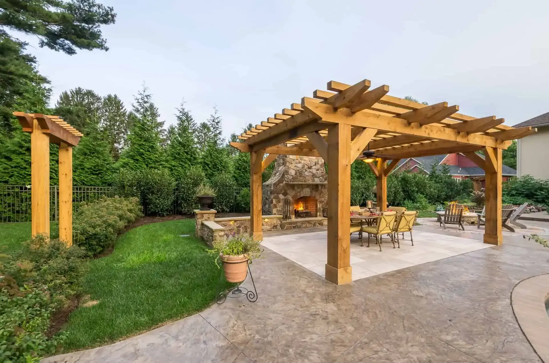 Backyard patio with wooden pergola, stone fireplace, and outdoor seating beside a garden lawn