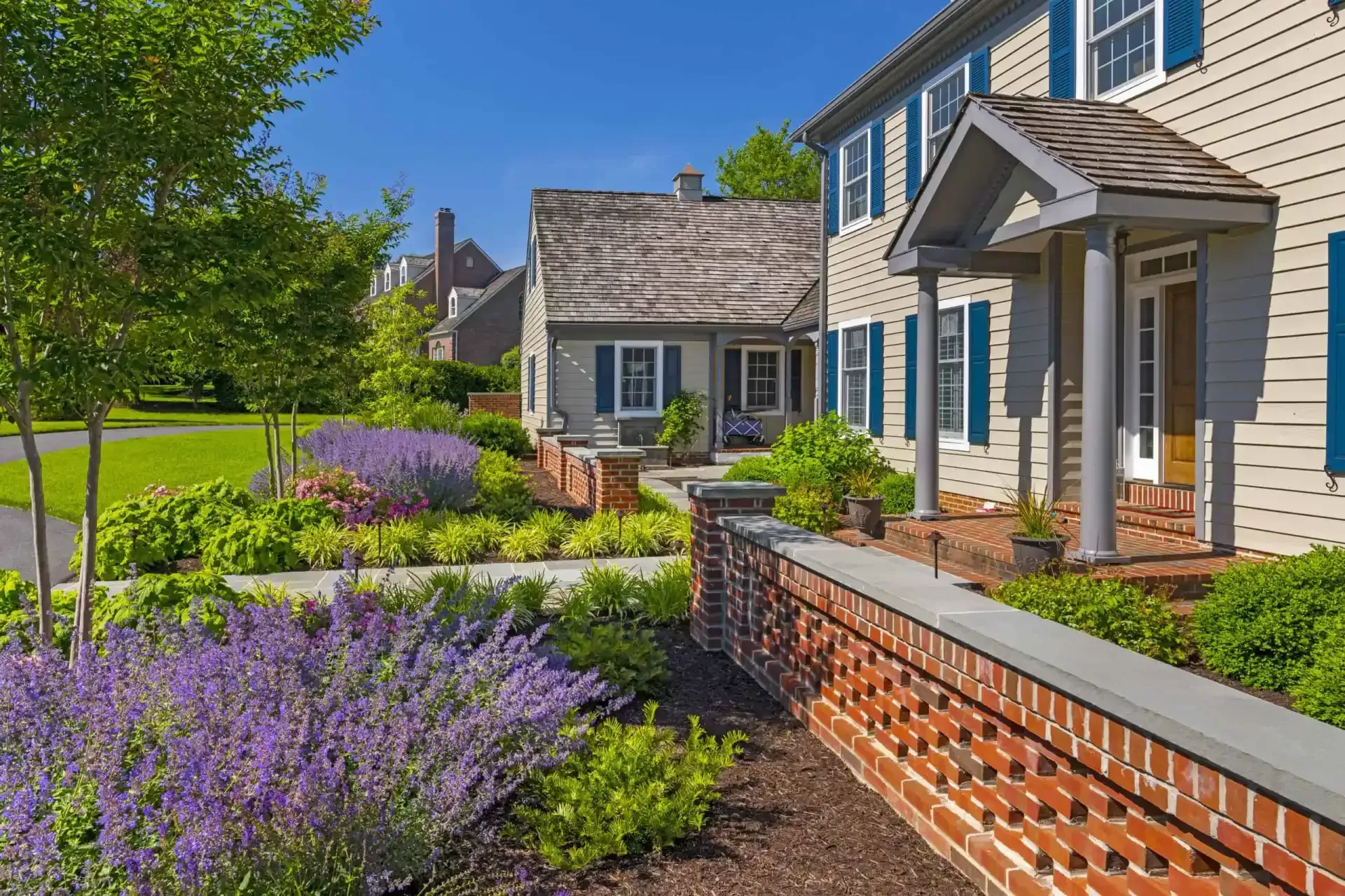 Suburban home with blue shutters, brick wall, and purple lavender garden in bright sunlight