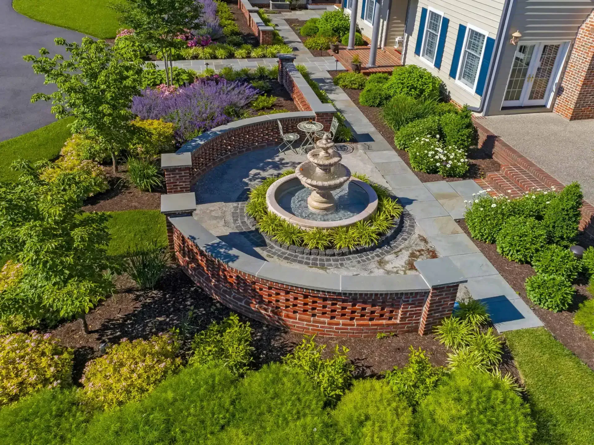 Aerial view of a landscaped courtyard with a central stone fountain, brick wall, and surrounding flowers and shrubs