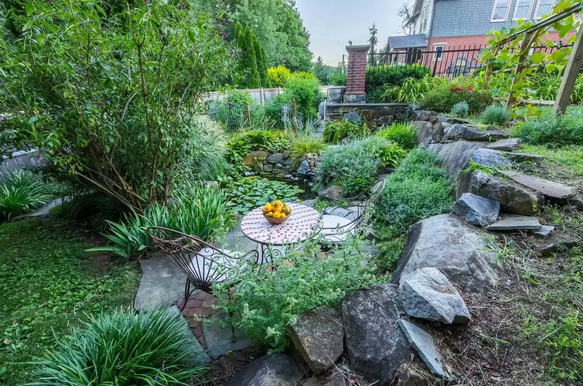 Lush garden with stone path, small round table, and rocks surrounding a leafy flower bed