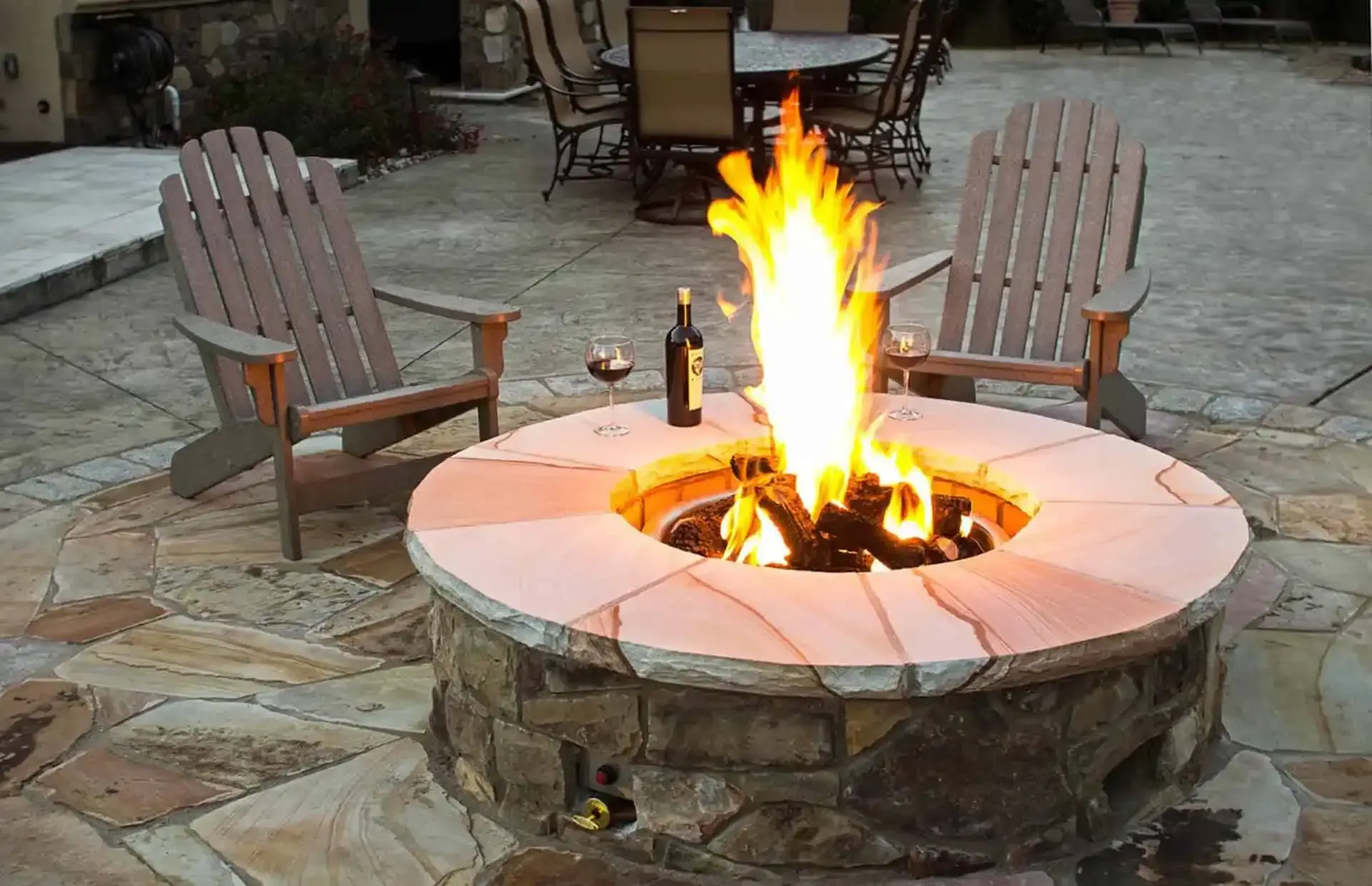 Stone fire pit with a bright flame, surrounded by two wooden chairs on a patio