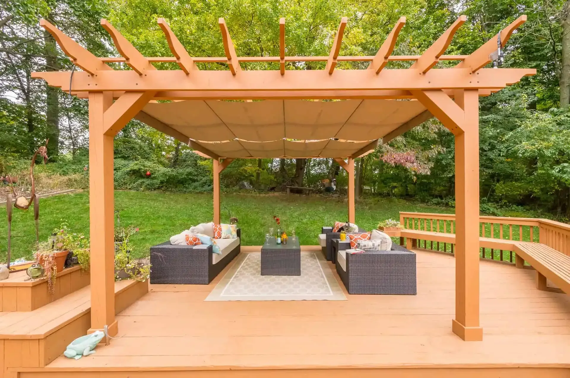 Wooden deck pergola with cushioned seating and a dining table in a green backyard garden